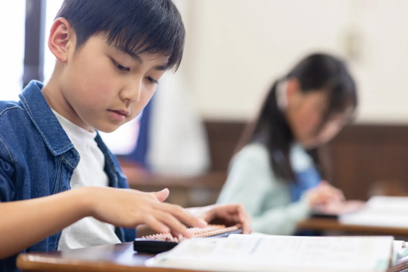 男の子がそろばんの練習をしているところを右側から見ている。その向こうに女の子もそろばんの練習をしている。
